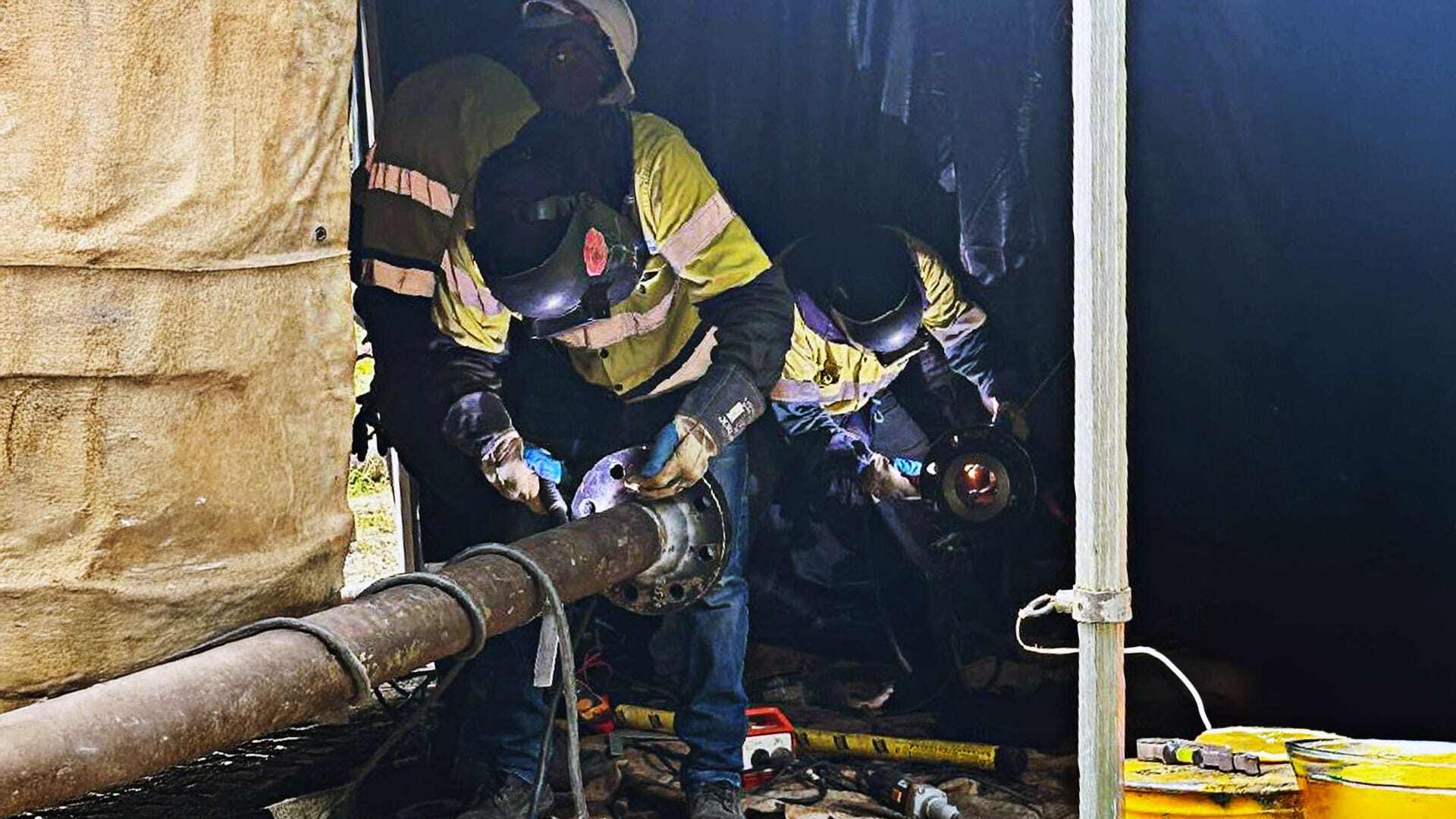 Team working in a tent welding parts to a pipe
